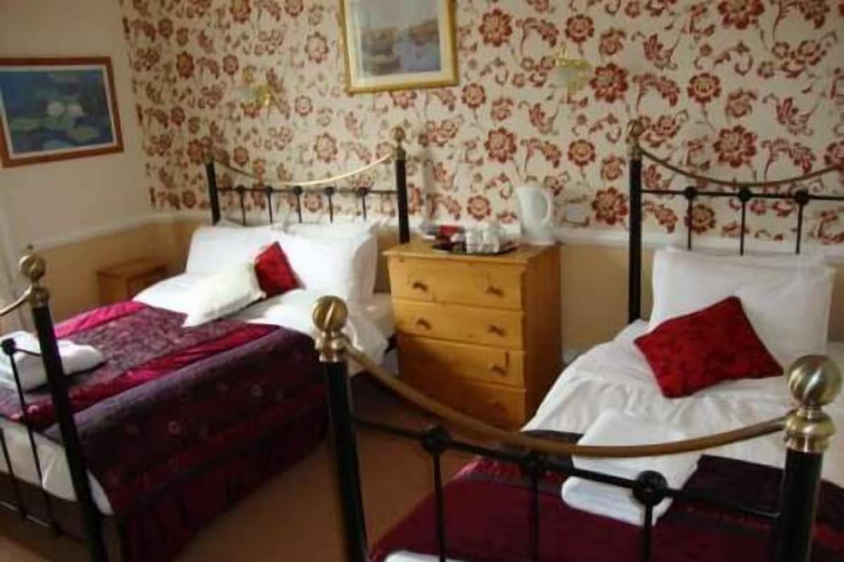 Ein Schlafzimmer mit zwei Einzelbetten, einer Holzkommode und blumigem Wandpapier.