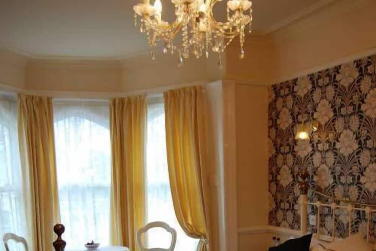 Ein Schlafzimmer mit einem großen Bett, einer Kandelaber, einem Esstisch mit Stühlen und einem Wandteppich mit Muster.