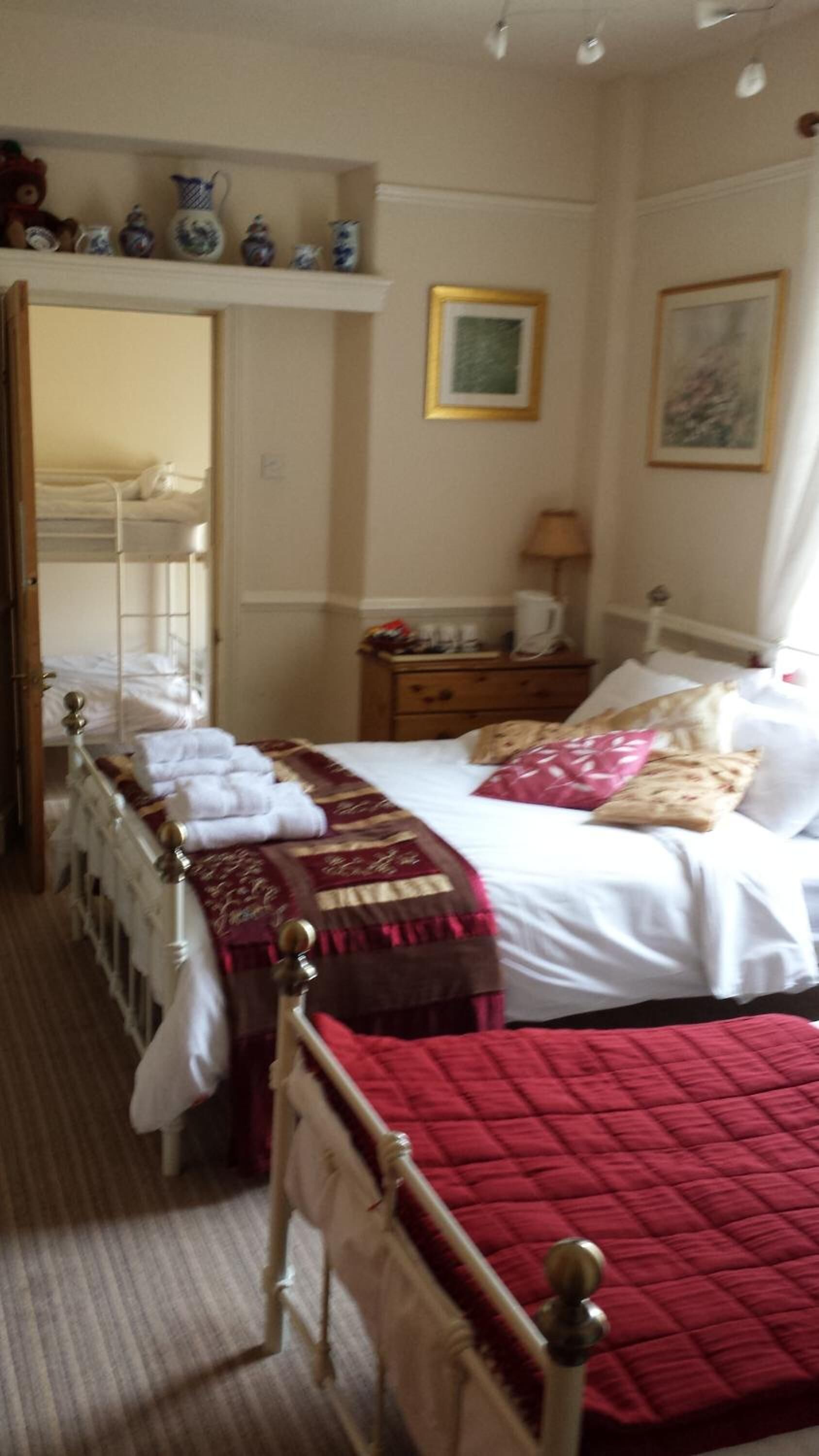 A hotel room with a bed, a nightstand, a lamp, a dresser, and a shelf with decorative items.