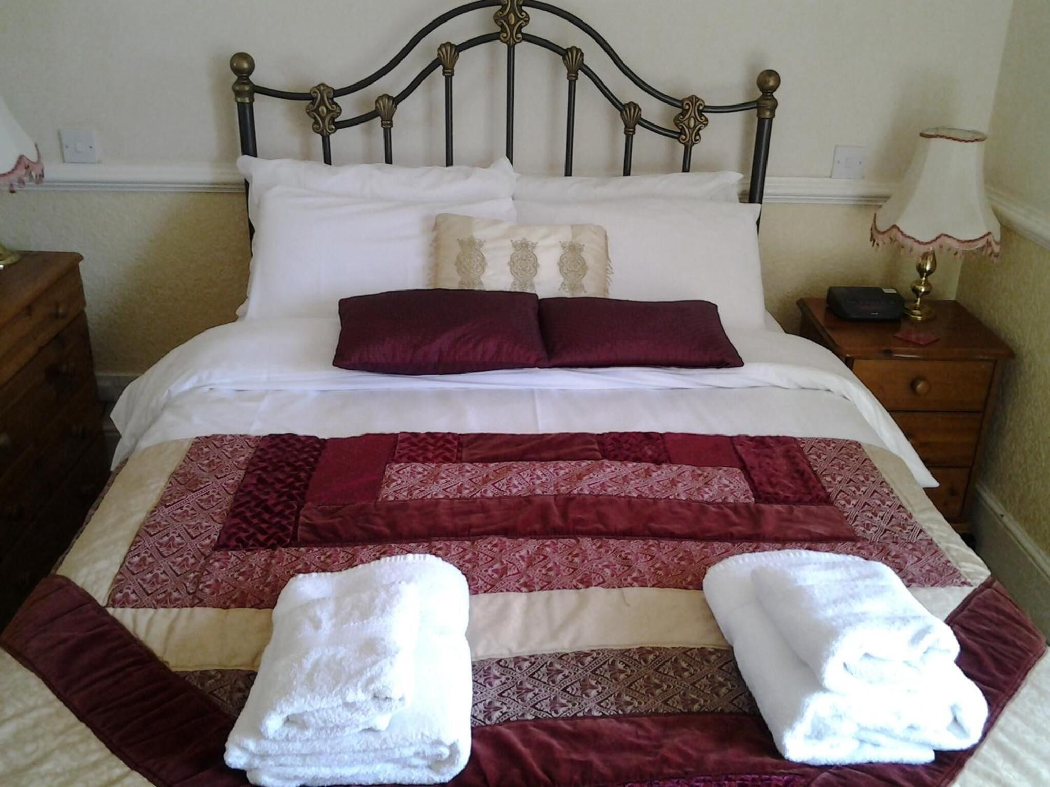A neatly made bed with a patterned quilt, two pillows, and two folded towels.