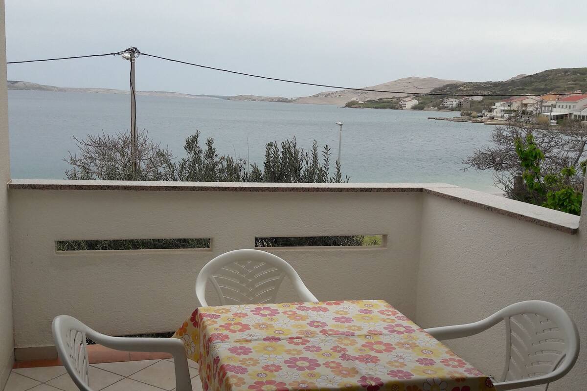 A balcony with a table and chairs, overlooking a body of water and a distant shoreline.
