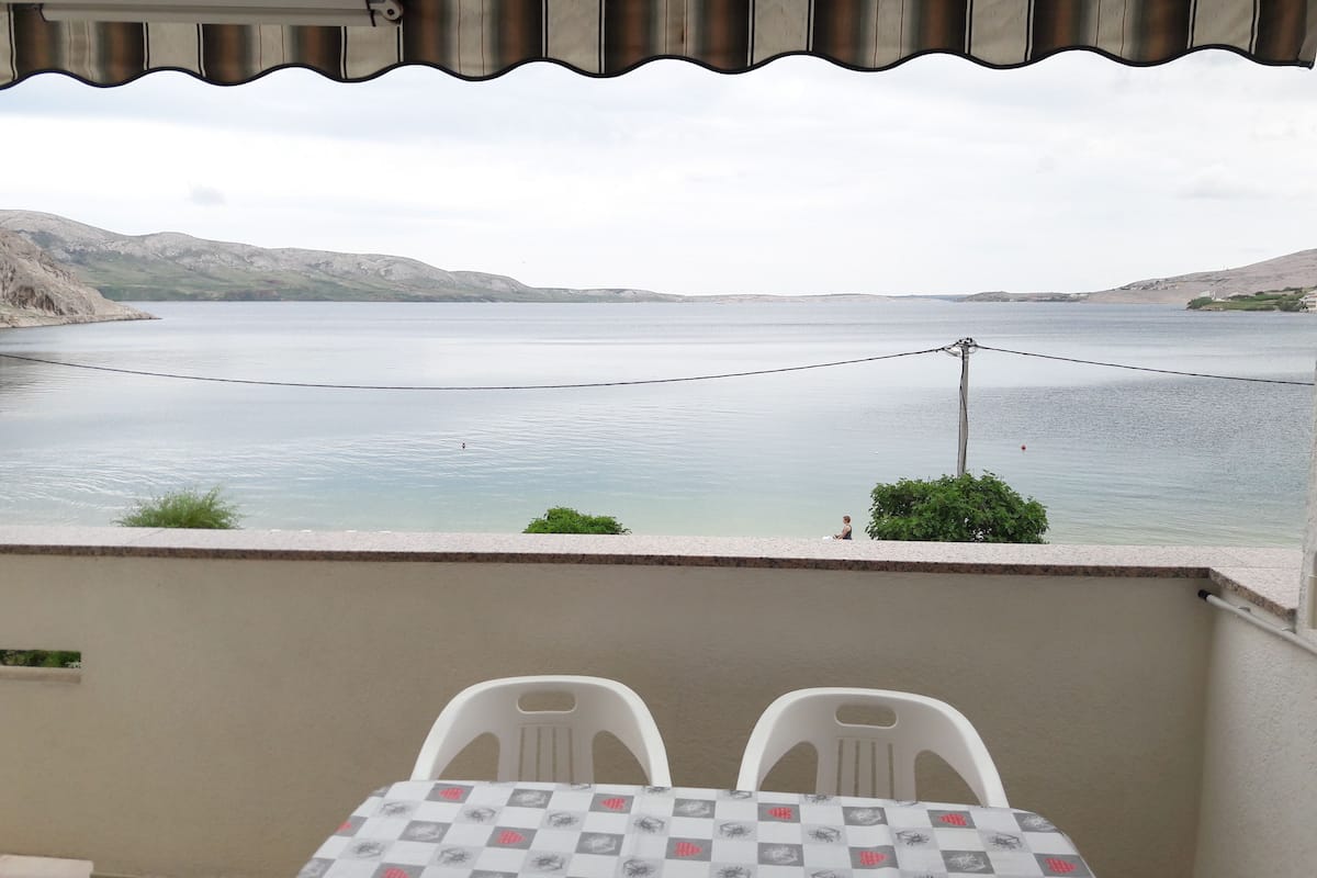 A balcony with a table and two chairs overlooking a calm lake, with mountains in the background.