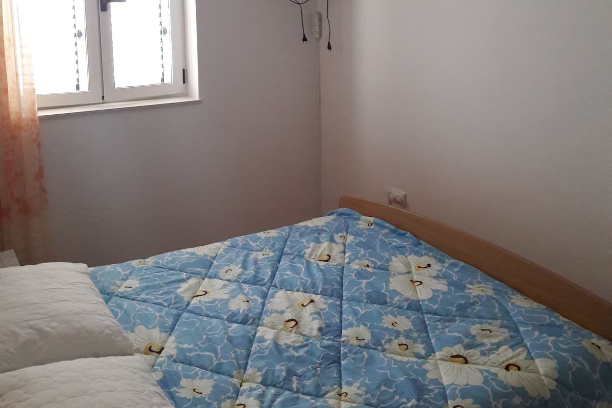 A bedroom with a bed, a television mounted on the wall, and an air conditioning unit above the bed.