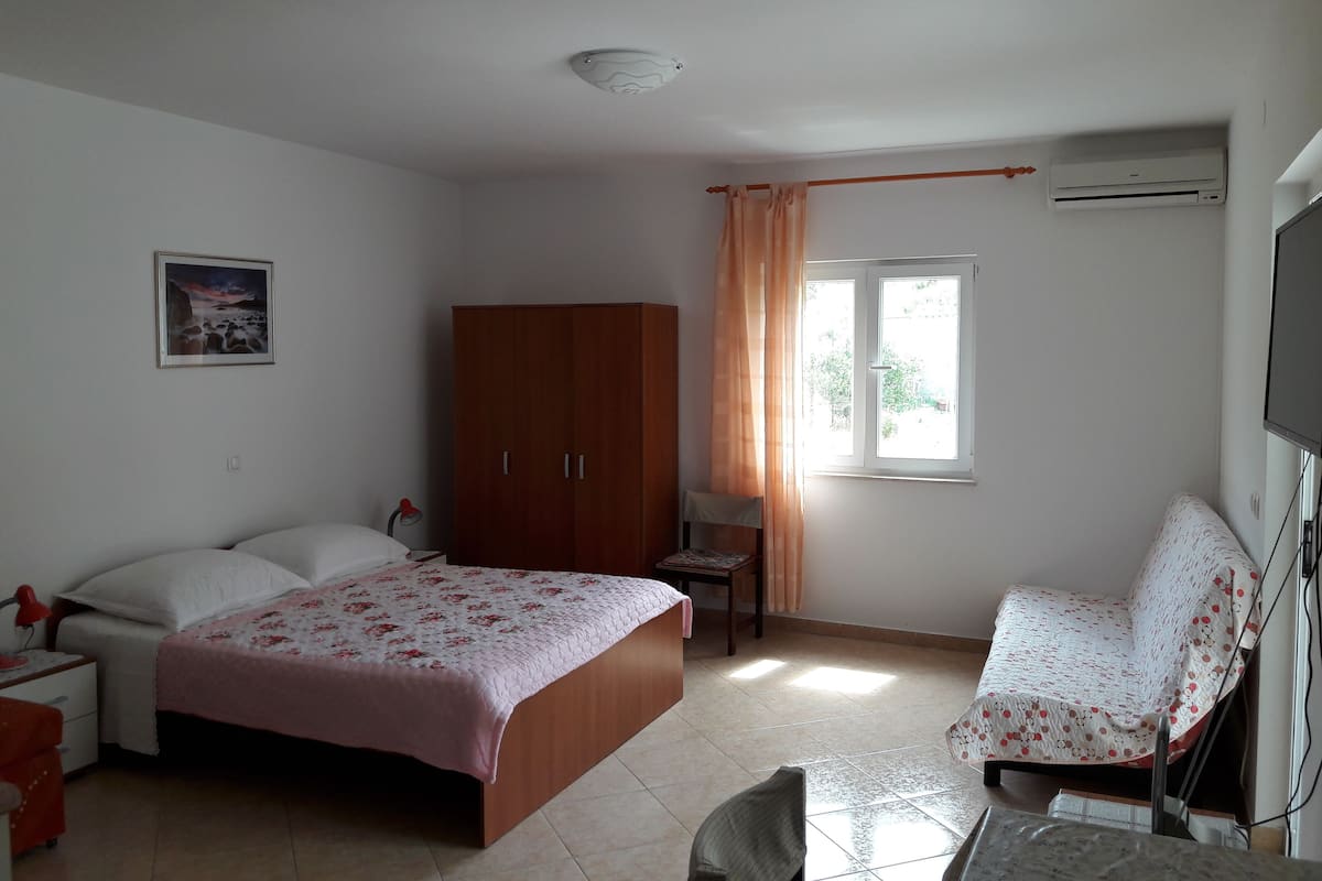 A bedroom with a bed, a wardrobe, a desk with a chair, and a window with curtains.