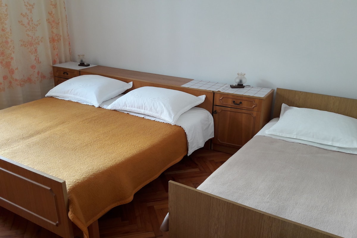 A room with two beds, wooden furniture, and a small desk with a lamp.
