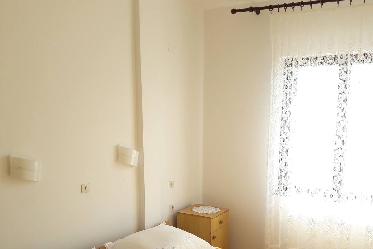 A bedroom with a bed, a nightstand, and a window with a curtain.