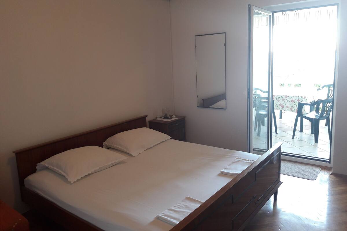 A bedroom with a bed, a nightstand, a mirror, and a sliding glass door leading to an outdoor area with chairs.