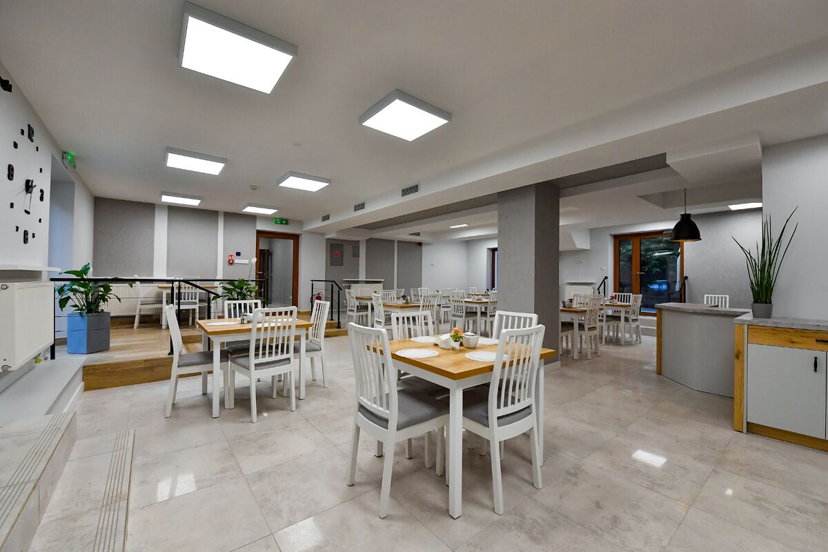 A spacious dining area with multiple tables and chairs, a kitchen area with a counter, and a staircase leading to an upper level.