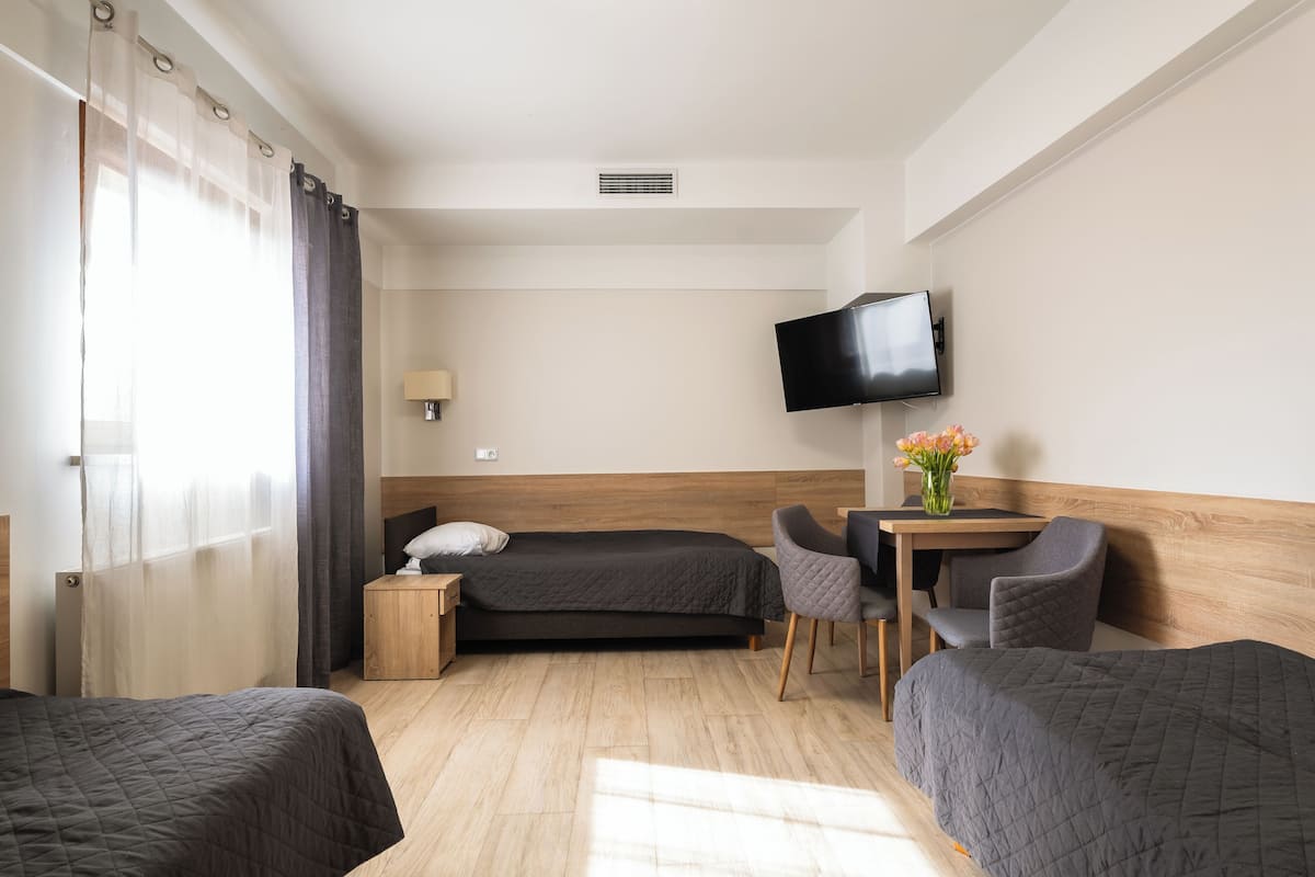 A hotel room with a bed, a desk with a chair, a TV, and a small table with a vase of flowers.