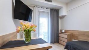 Habitación de hotel con una mesa de madera, un jarrón de flores, una cama, un aparador y un televisor en la pared.