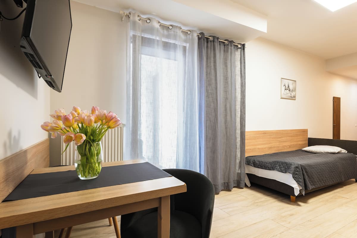 A hotel room with a bed, a table with a vase of flowers, a television, and a window with curtains.