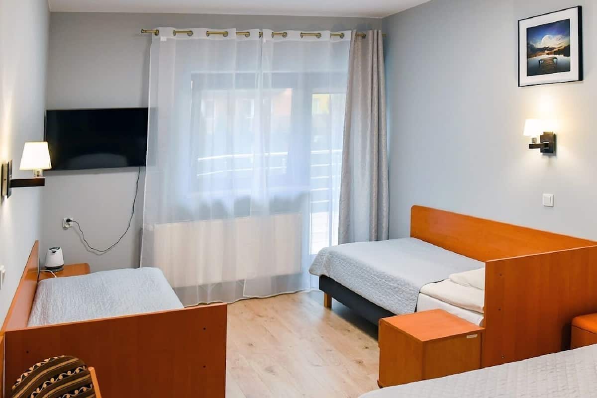 A hotel room with two beds, a TV, a lamp, and a window with curtains.
