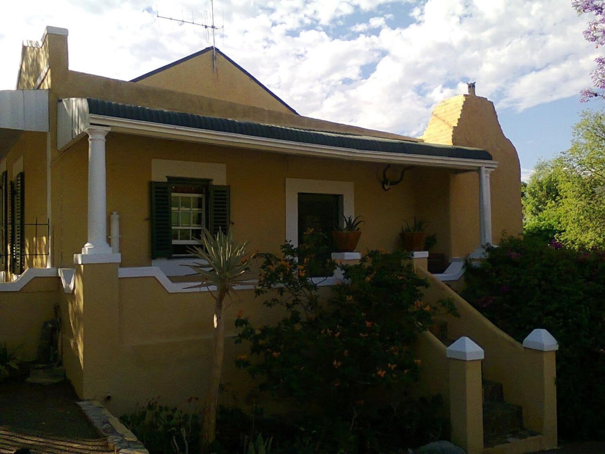 A yellow house with a gabled roof, white trim, and a small porch with potted plants.