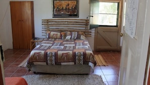 Une chambre à coucher avec un lit en bois, un tableau encadré au mur et une porte avec une fenêtre.