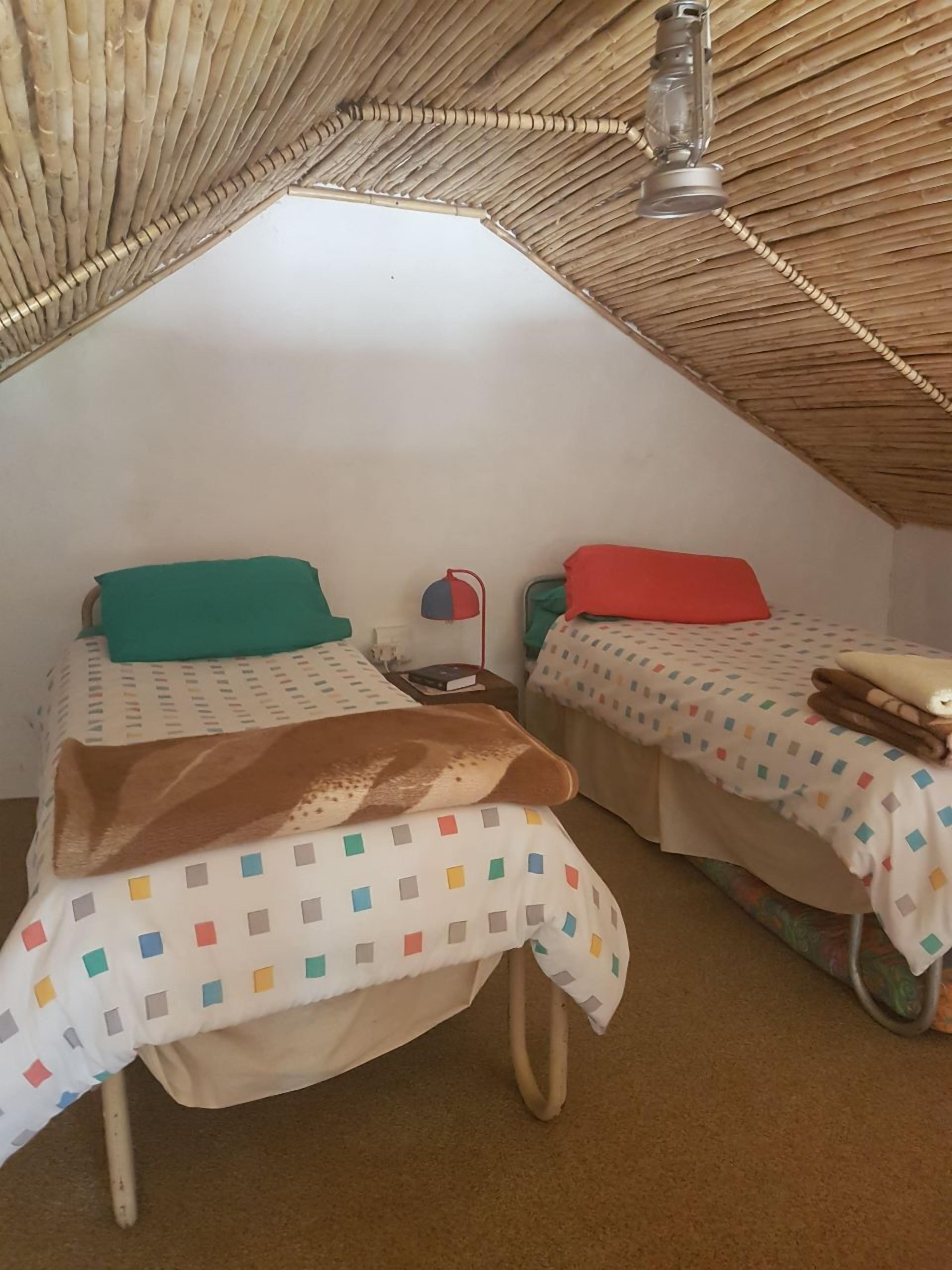 A small attic room with two beds, a hanging light fixture, and a woven ceiling.