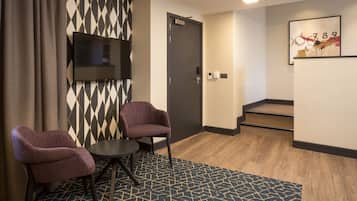Habitación de hotel con televisión montada en la pared, dos sillones, una mesita y una alfombra estampada.