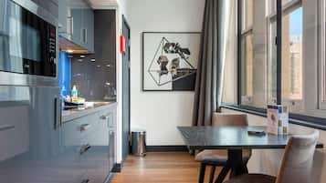 Een moderne keuken met roestvrijstalen apparatuur, een eethoek met een tafel en stoelen, en een lijstwerk met abstracte geometrische vormen aan de muur.
