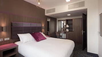 A hotel room with a large bed, a desk, a chair, and a wardrobe.