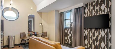 Quarto de hotel com sofá, televisão, espelho e parede estampada.