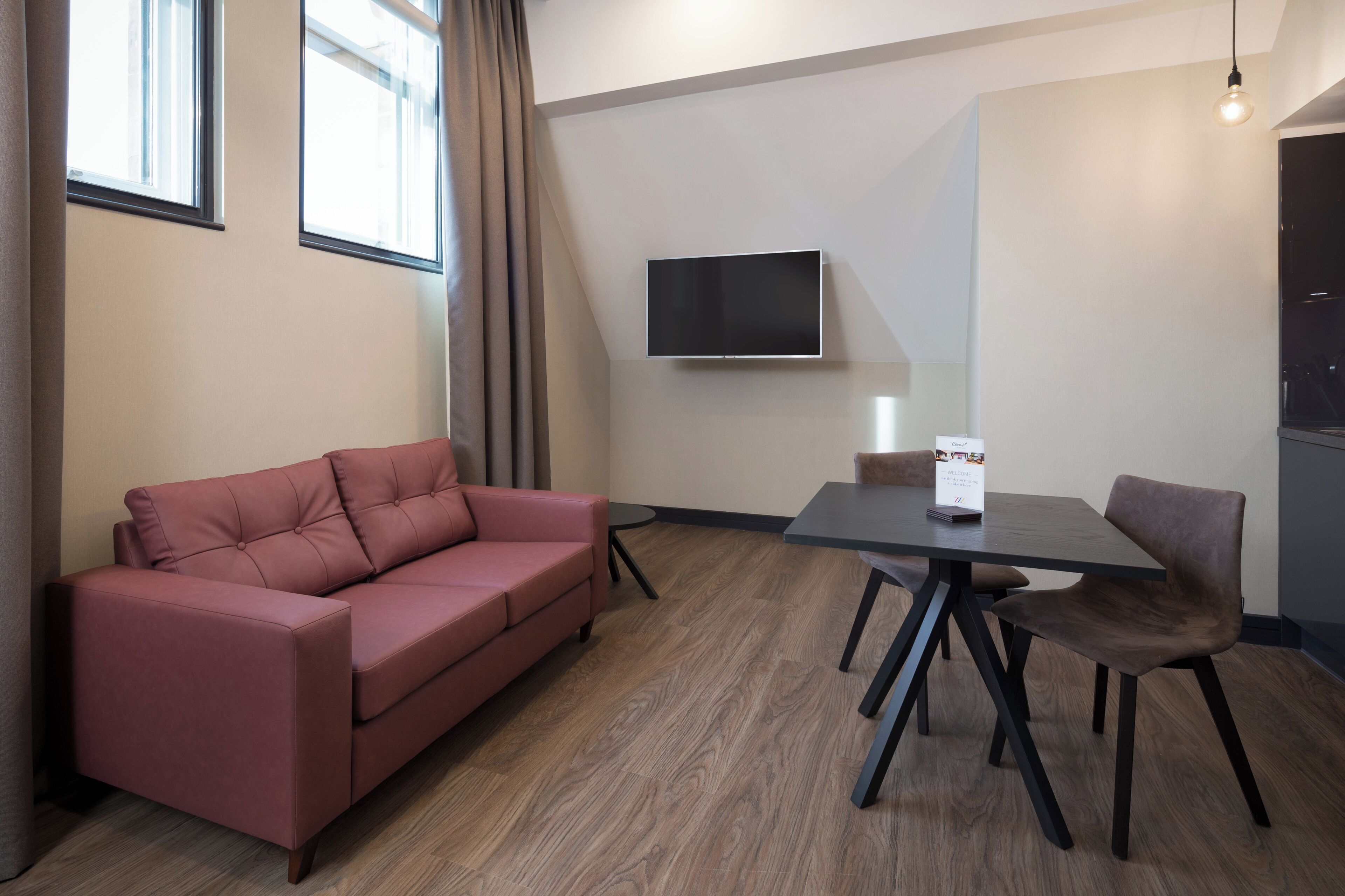 A modern room with a red sofa, a dining table with chairs, a flat-screen TV mounted on the wall, and a wooden floor.
