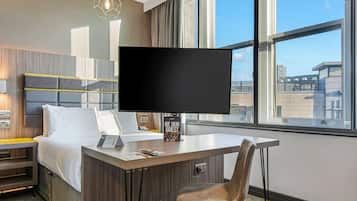 Habitación de hotel con cama, escritorio, silla, televisión de pantalla plana y ventana con vista a la ciudad.