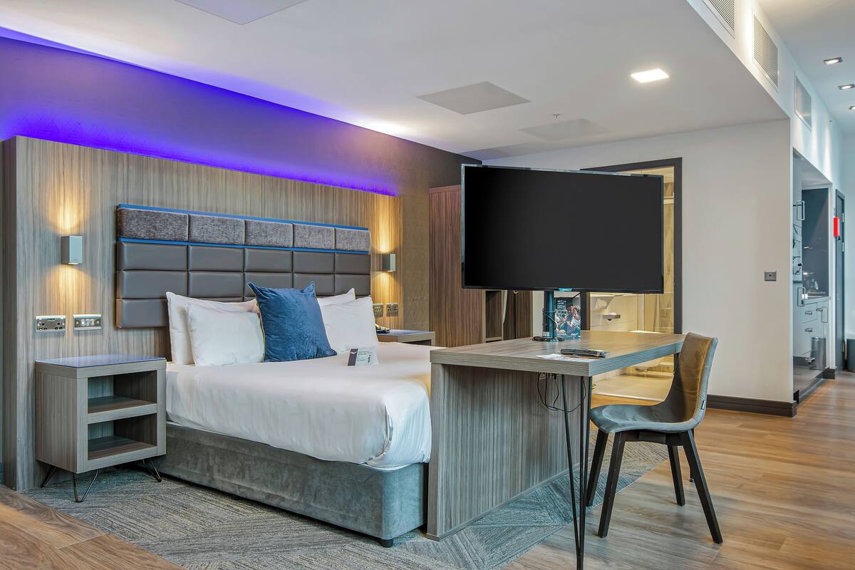 A modern hotel room with a bed, bedside tables, a desk, and a TV.