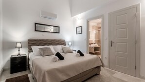Un dormitorio con cama, mesitas de noche, un espejo y una puerta que da al baño.