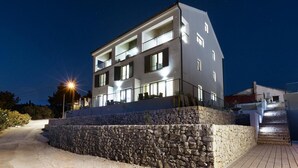 Un edificio moderno de dos pisos con base de piedra, varios balcones y fachada bien iluminada.