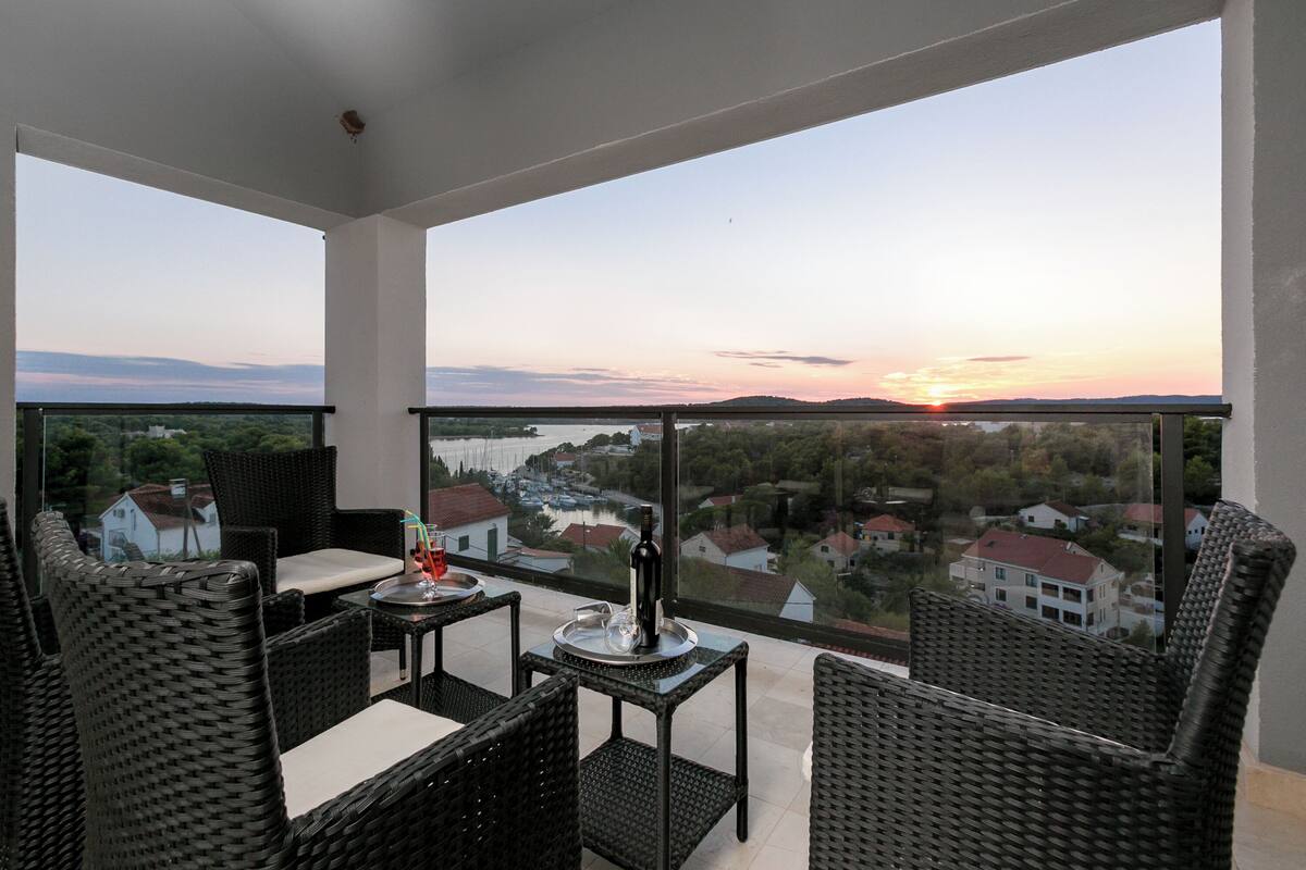 Ein Balkon mit Korbmöbeln, einem Tisch und einer Flasche.