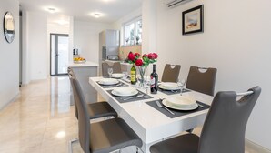 Comedor moderno con una mesa larga dispuesta para cuatro, cocina al fondo y un cuadro en la pared.