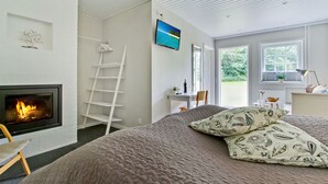 Une chambre avec une cheminée, un lit agrémenté d’oreillers à motifs, un téléviseur fixé au mur et une vue sur la verdure à l’extérieur.