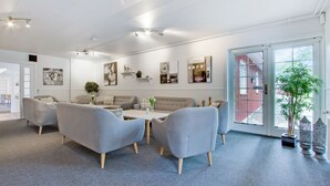 Un salon moderne comprenant un ensemble de canapés, une table basse et une table à manger. On y trouve des étagères murales ornées d’objets décoratifs, ainsi qu’une grande fenêtre donnant sur l’extérieur.