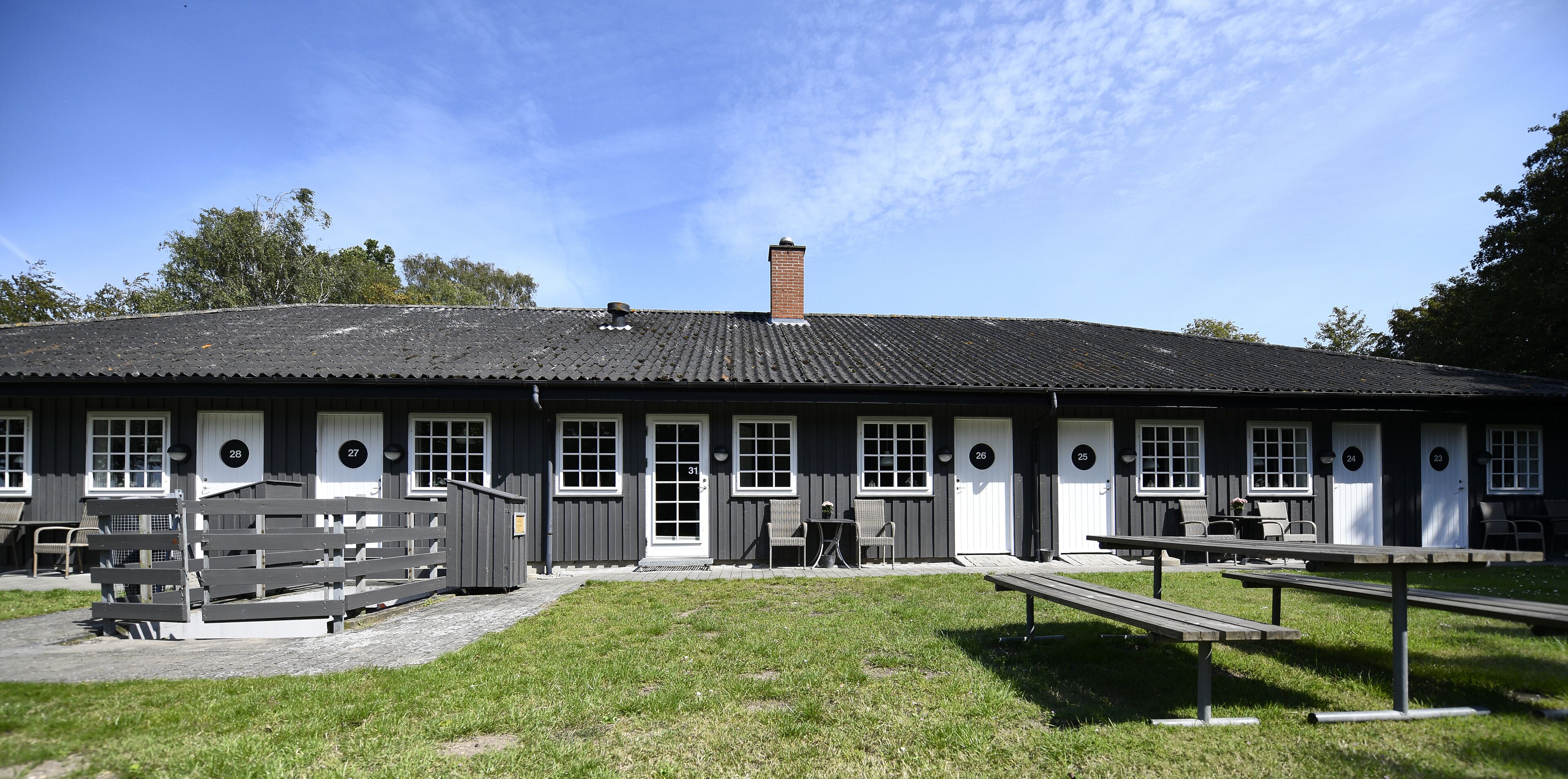 A building with numbered doors, outdoor seating, and a grassy area.