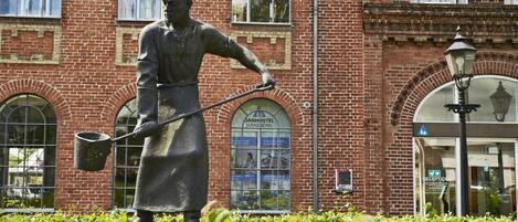 A statue of a man holding a shovel in front of a brick building with arched windows and a sign that reads "DANHOSTEL SVENDBORG".