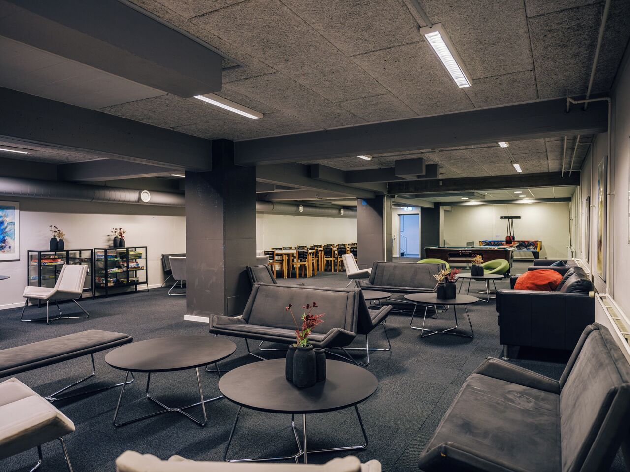 A modern waiting area with seating, tables, and a bookshelf.