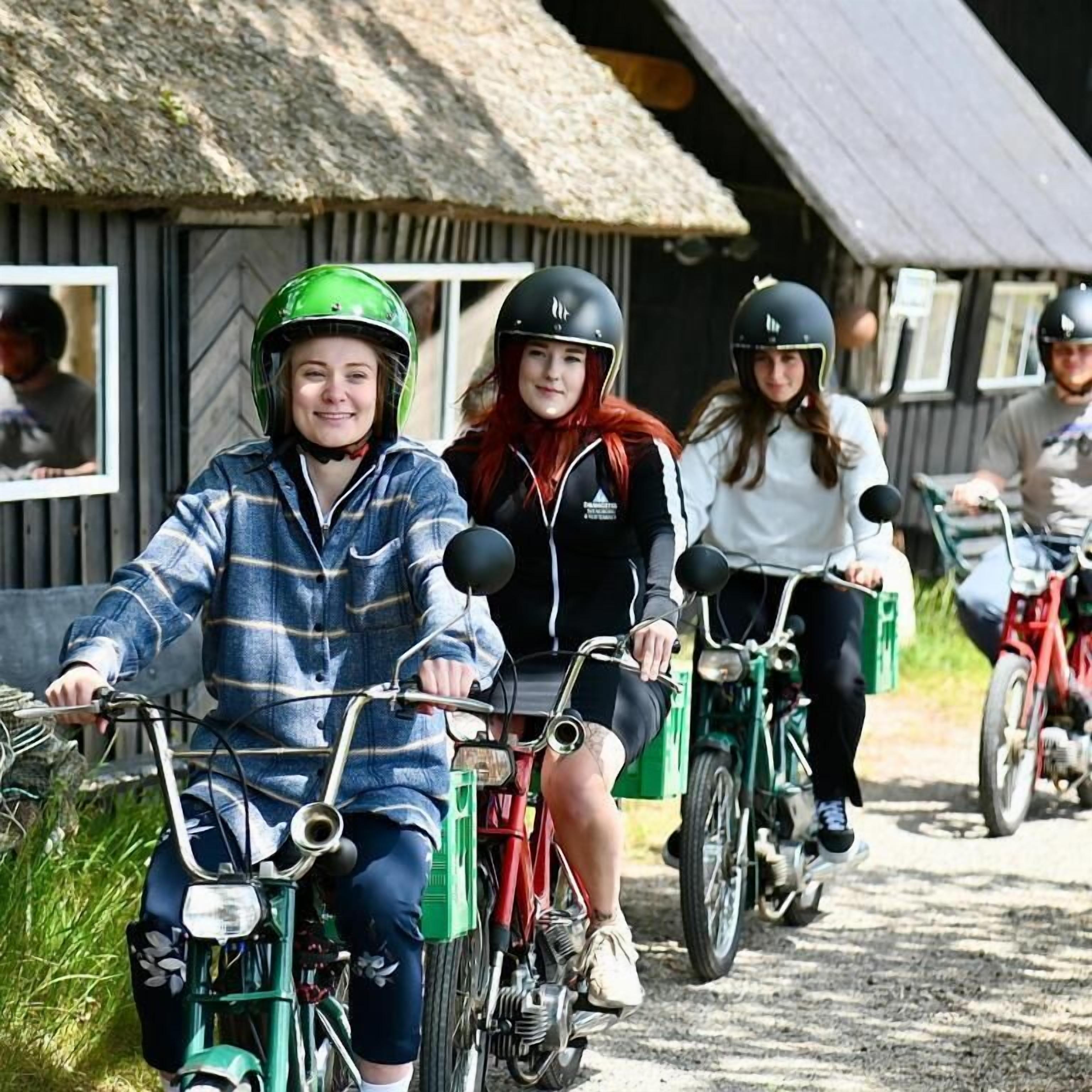 Un grupo de personas en bicicleta en un entorno rural con edificios de techo de paja.