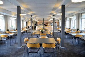 A spacious dining area with multiple tables and chairs, a central kitchen area, and large windows allowing natural light. - Stoeberiet (Svendborg)