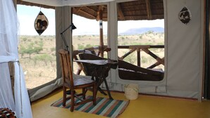 A room with a wooden chair, a small table, a lamp, and a view of the desert landscape.