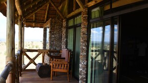 A wooden deck with a stone pillar, a wooden chair, and a large window overlooking a landscape.