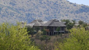 A house with a thatched roof, surrounded by sparse vegetation and a hill in the background.
