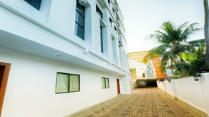 A corridor with a white building, a brick floor, and a palm tree. - Green Park residency (Kannur)