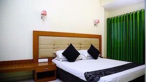 A neatly made bed with a wooden headboard, a bedside table, and a green curtain. - Green Park residency (Kannur)