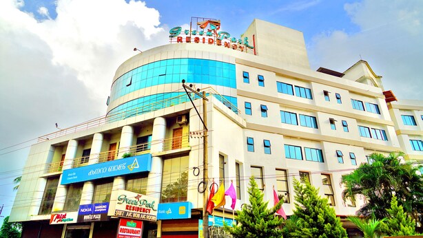 A multi-story building with a curved facade, a sign reading "Green Park Residency," and several commercial signs below. - Green Park residency (Kannur)