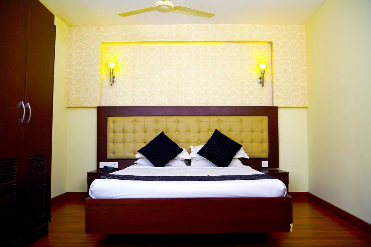 A hotel room with a large bed, a wooden headboard, two wall-mounted lamps, and a ceiling fan.