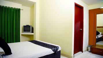 A bedroom with a bed, a television on a shelf, a red door, and a mirror.