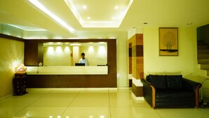 A hotel reception area with a reception desk, a black leather sofa, and a framed artwork on the wall. - Green Park residency (Kannur)