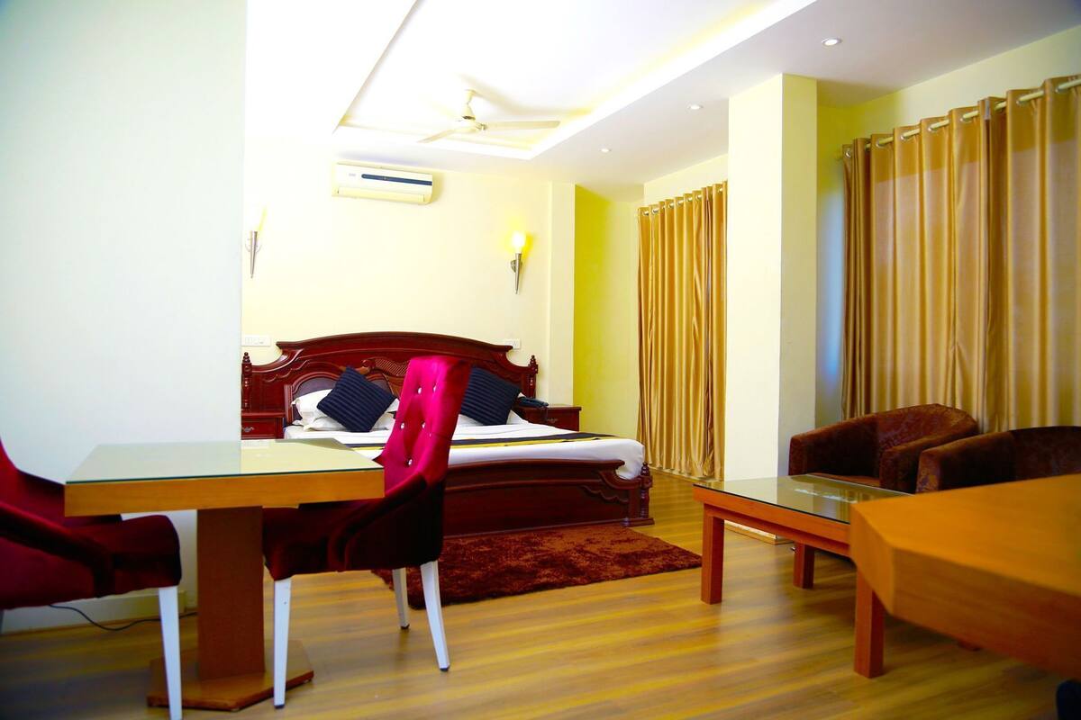 A hotel room with a bed, a desk, a chair, a sofa, and a curtain.