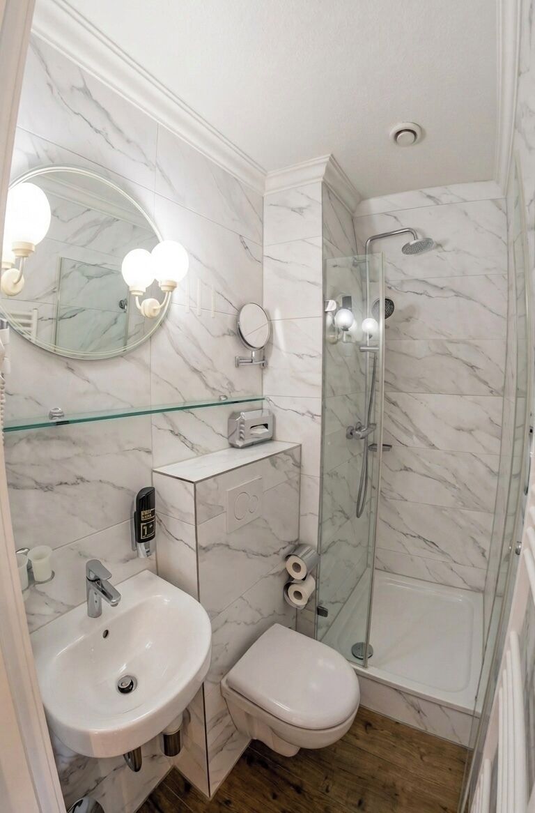 Ein Badezimmer mit Marmorwand, einer Duschkabine aus Glas, einem weißen Waschbecken und einer Toilette.
