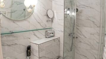 Un baño con pared de mármol, cabina de ducha de vidrio, lavamanos blanco y un inodoro.