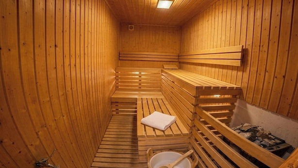 A wooden sauna with benches and a bench seat, a towel, and a bucket.